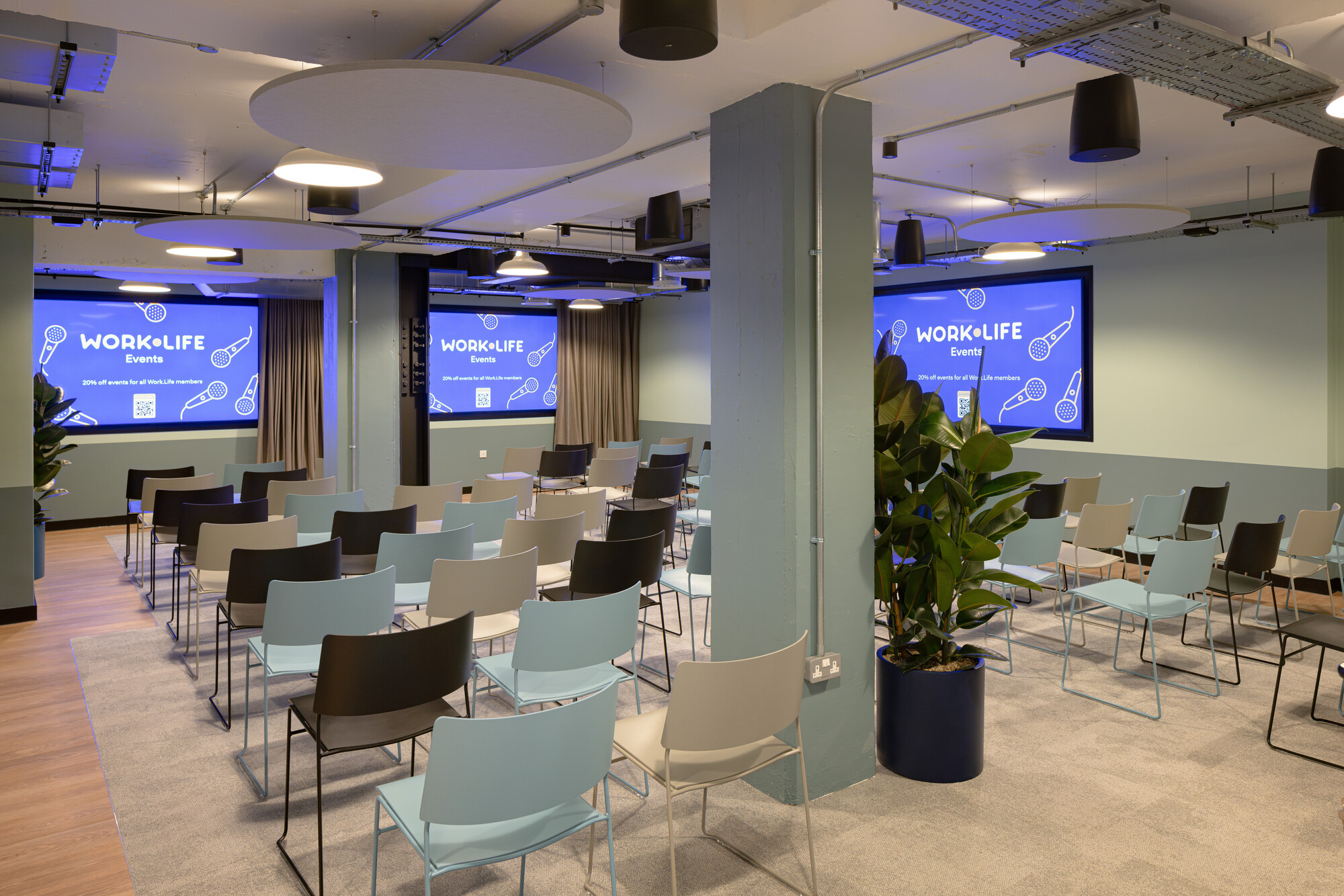 Work.Life Courtyard Building featuring the bespoke events room, with screens displaying the brand's logo, coloured seating options, and ceiling-to-floor curtains.