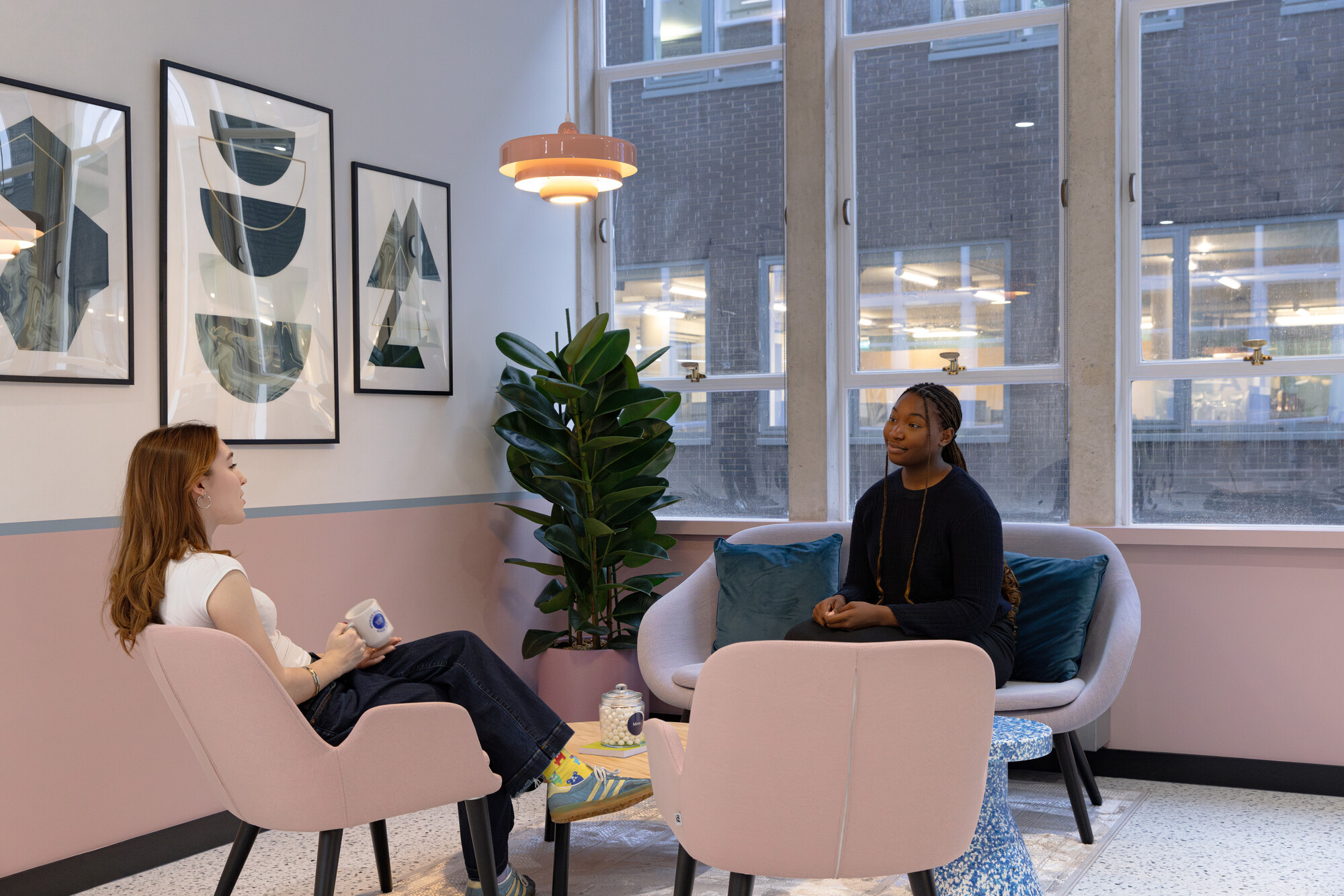 Work.Life Courtyard Building with two employees in a meeting, on soft pink seating, in an open space of the teapoint.