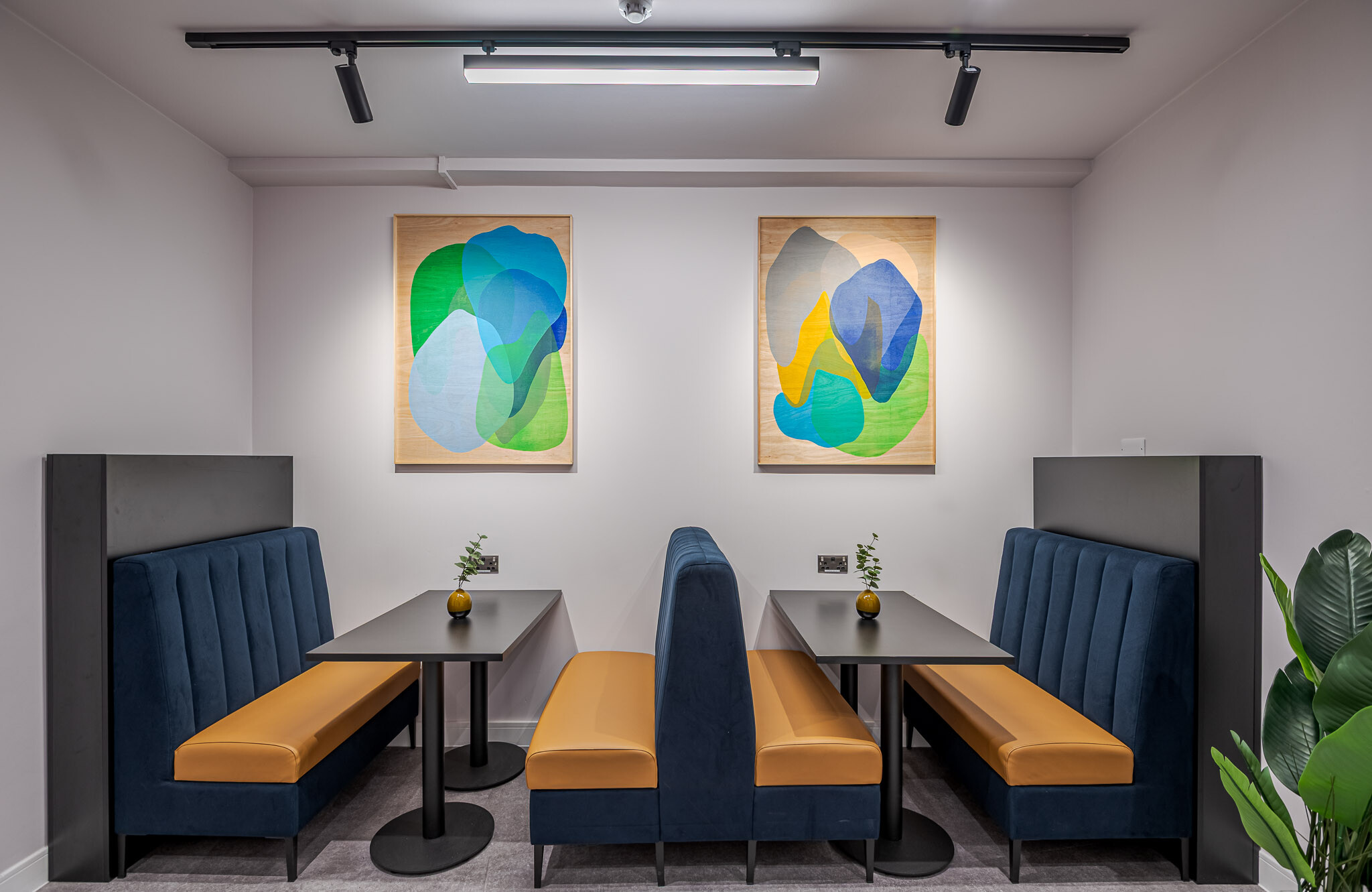 141 Fenchurch close-up of the breakout space at Alchemy Asset Management, highlighting two facing booths with plush navy seats, mustard cushions, and black tables. Small decorative vases and abstract artwork on the wall complete the modern look.