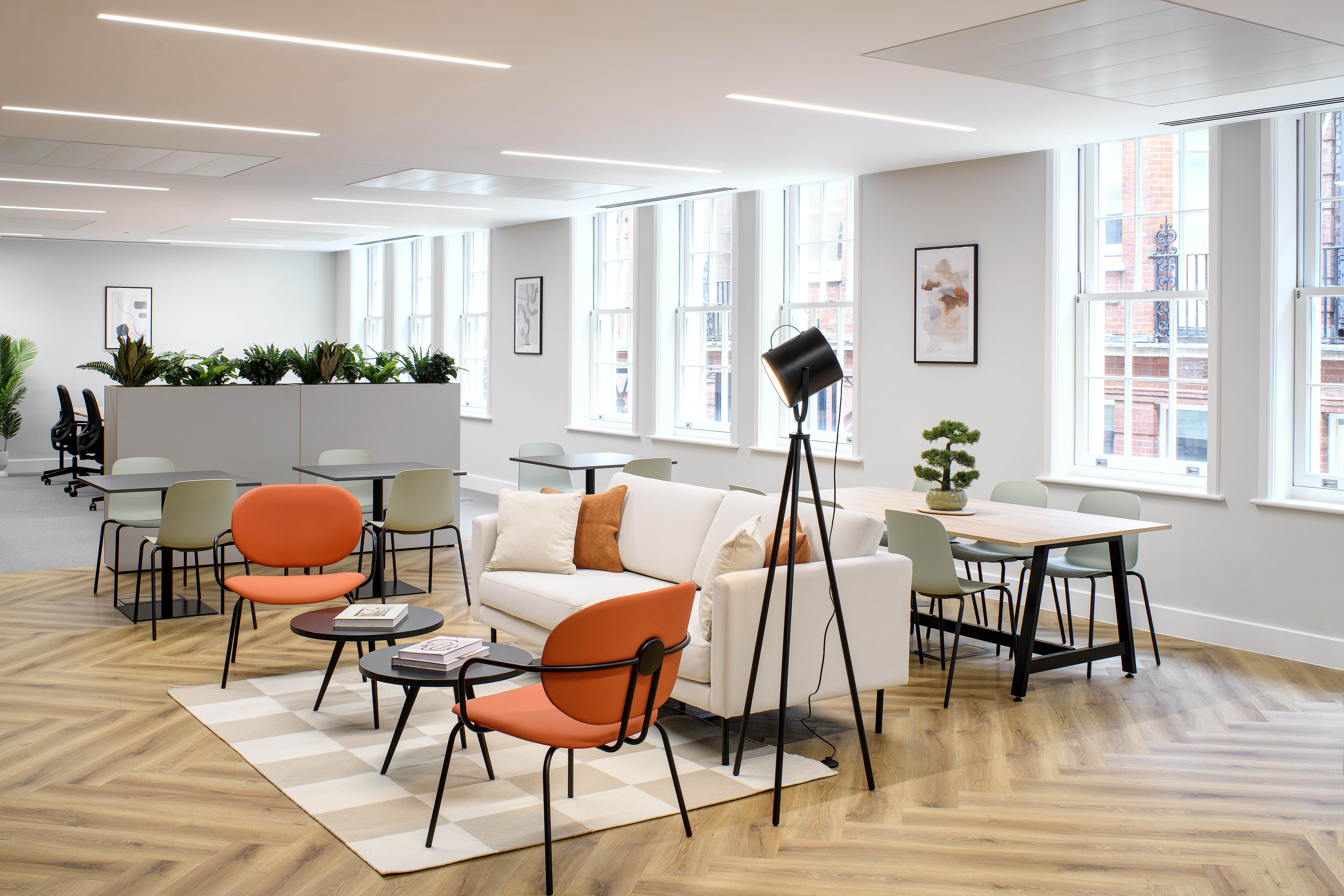 Assets Management Firm soft seating area, featuring orange and sage seats and cushions. This is a very bright and airy space, accompanied with large windows.