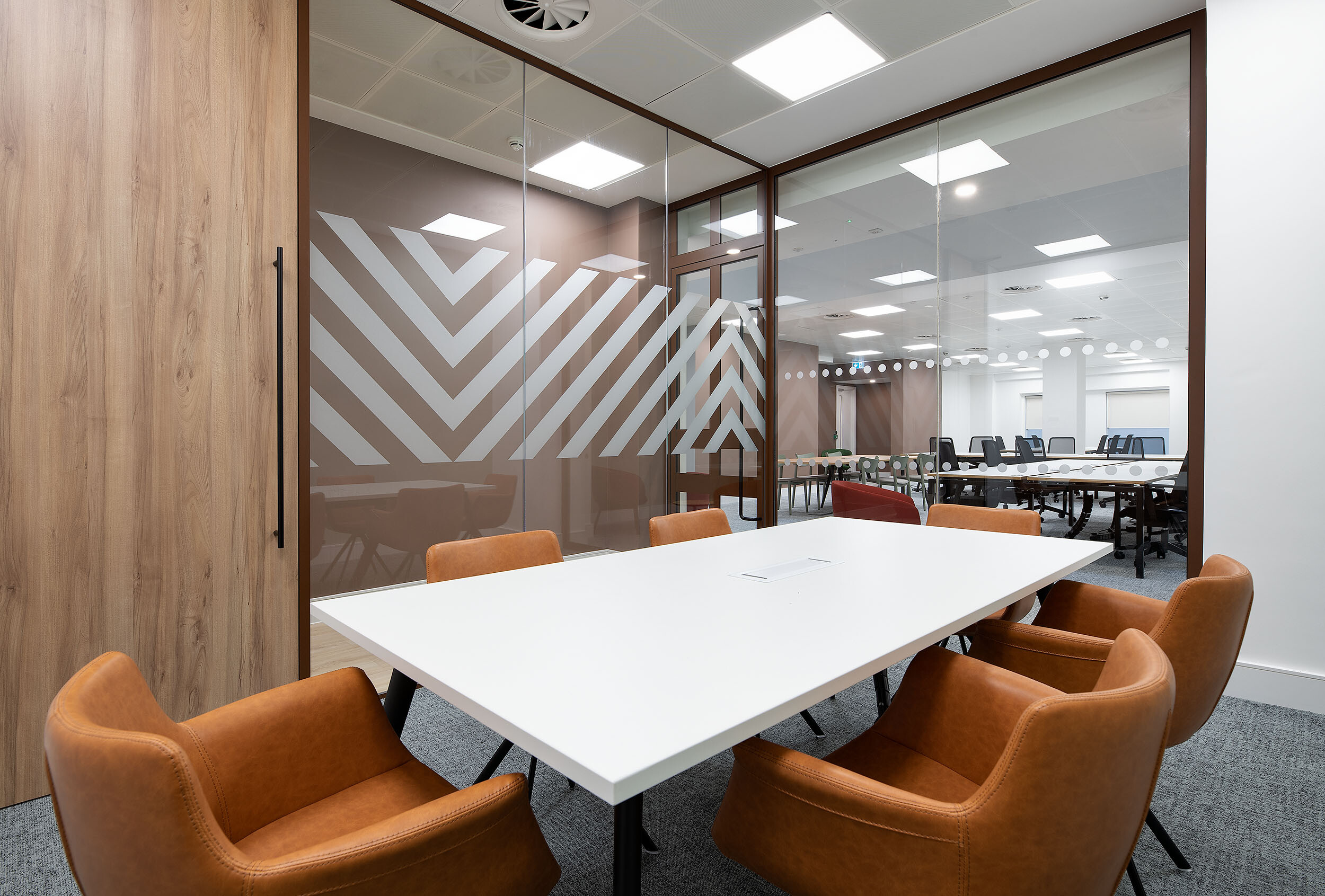A contemporary meeting room at 123 Pall Mall, with leather chairs, a white table, and glass walls with bespoke geometric manifestation that provides privacy.