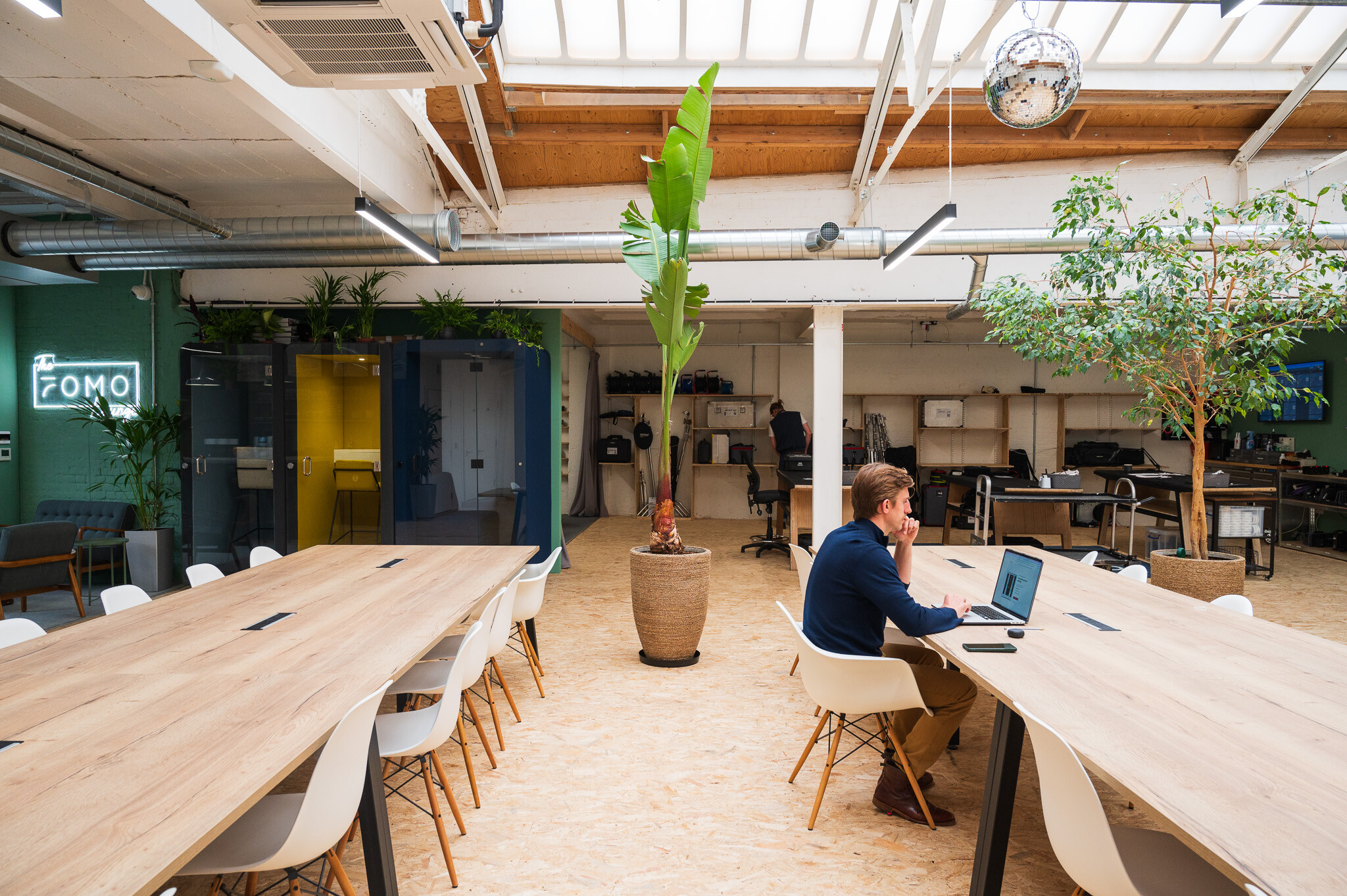 A collaborative office layout at FOMO Rentals by Two, with long wooden tables, ergonomic chairs, and natural greenery enhancing the workspace atmosphere.