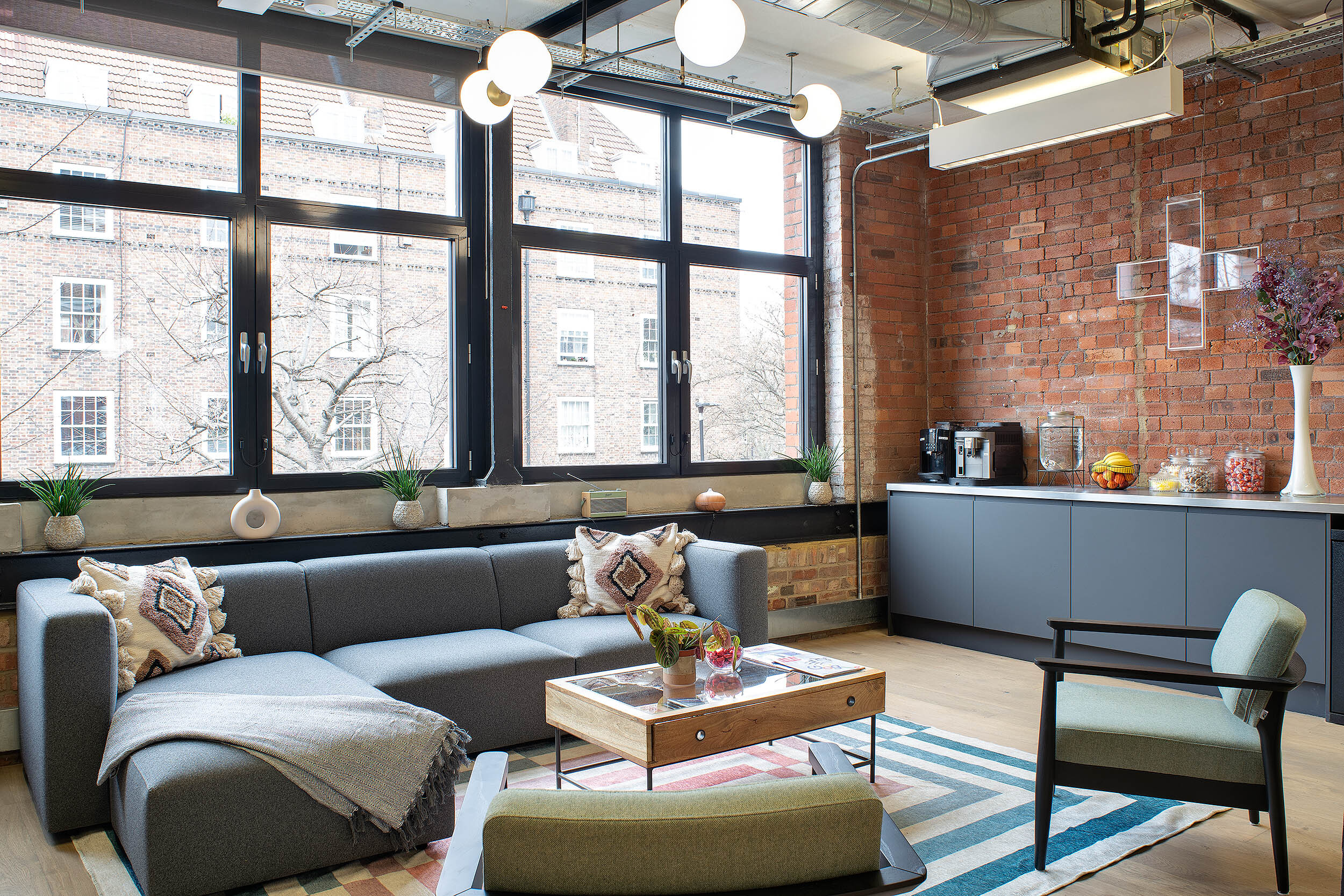 Cosy breakout area at the Kin & Carta office designed by Two, featuring a modern sofa, exposed brick walls, and a teapoint with coffee facilities.