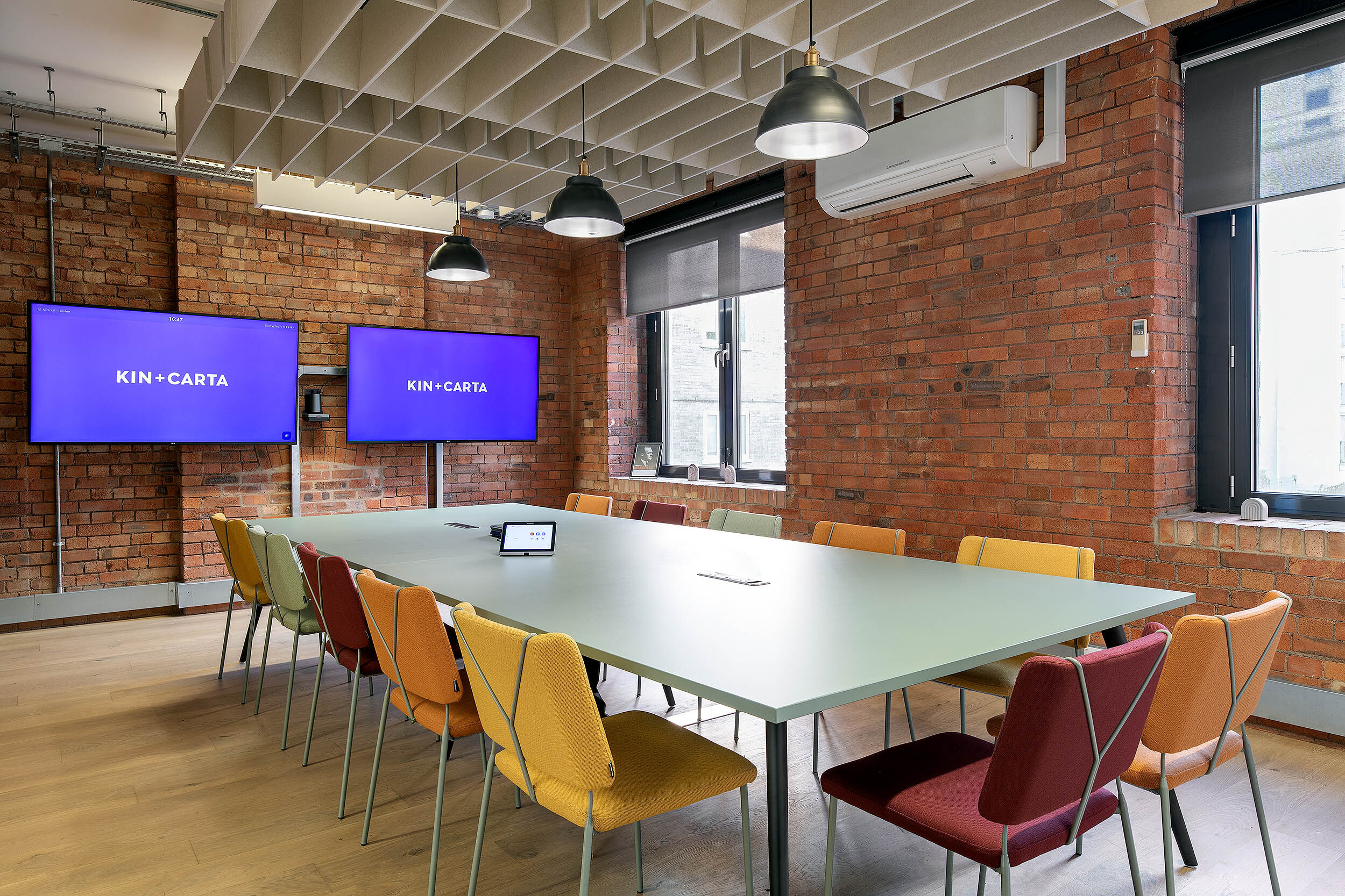 Modern meeting room at the Kin & Carta office, designed by Two, with colourful chairs, a central table, and dual screens for presentations.
