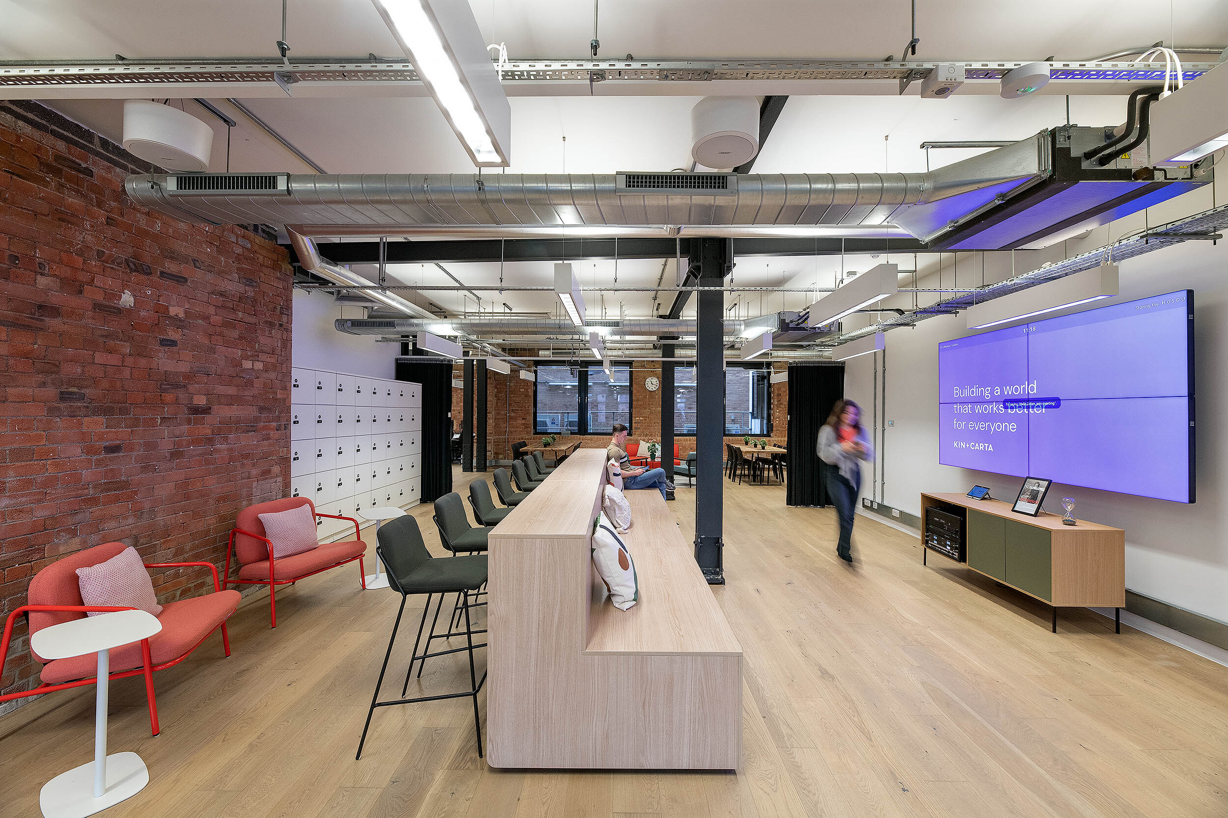 Comfortable seating area at Kin & Carta, designed by Two, with red armchairs, a modern bench, and natural wooden flooring in an industrial-style setting.
