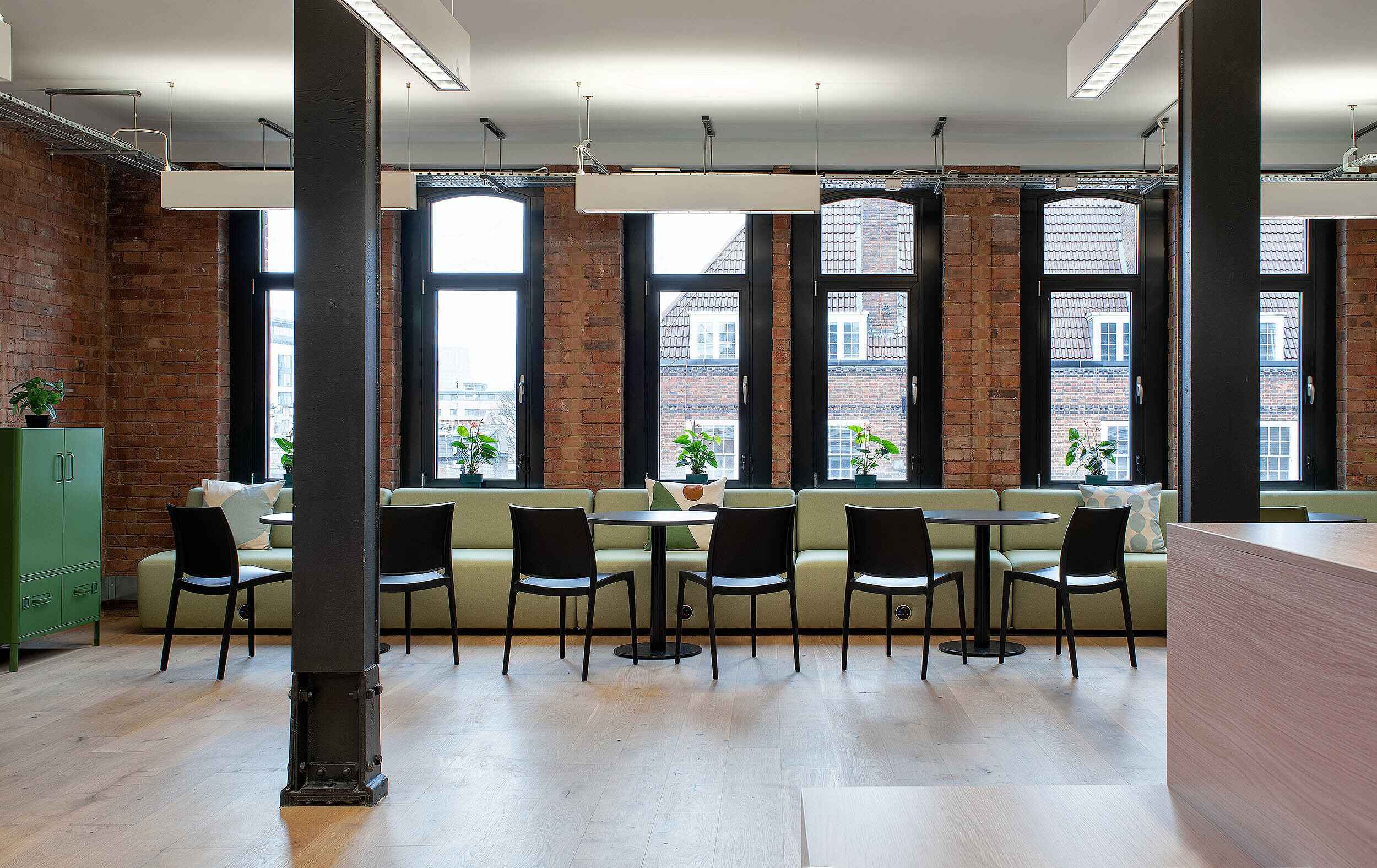 A bright office lounge designed by Two, with light green sofas, black chairs, and large windows overlooking the surrounding city.