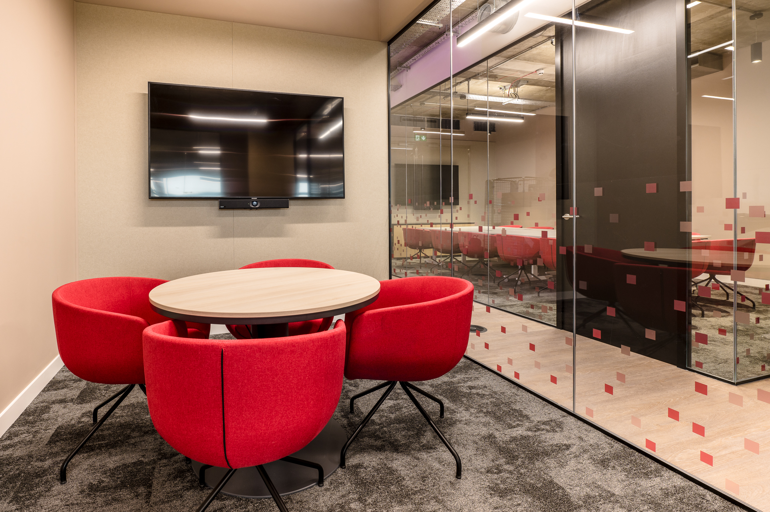 A private meeting room in the MicroStrategy office designed by Two, featuring vibrant red chairs, a round table, and a wall-mounted screen for presentations.