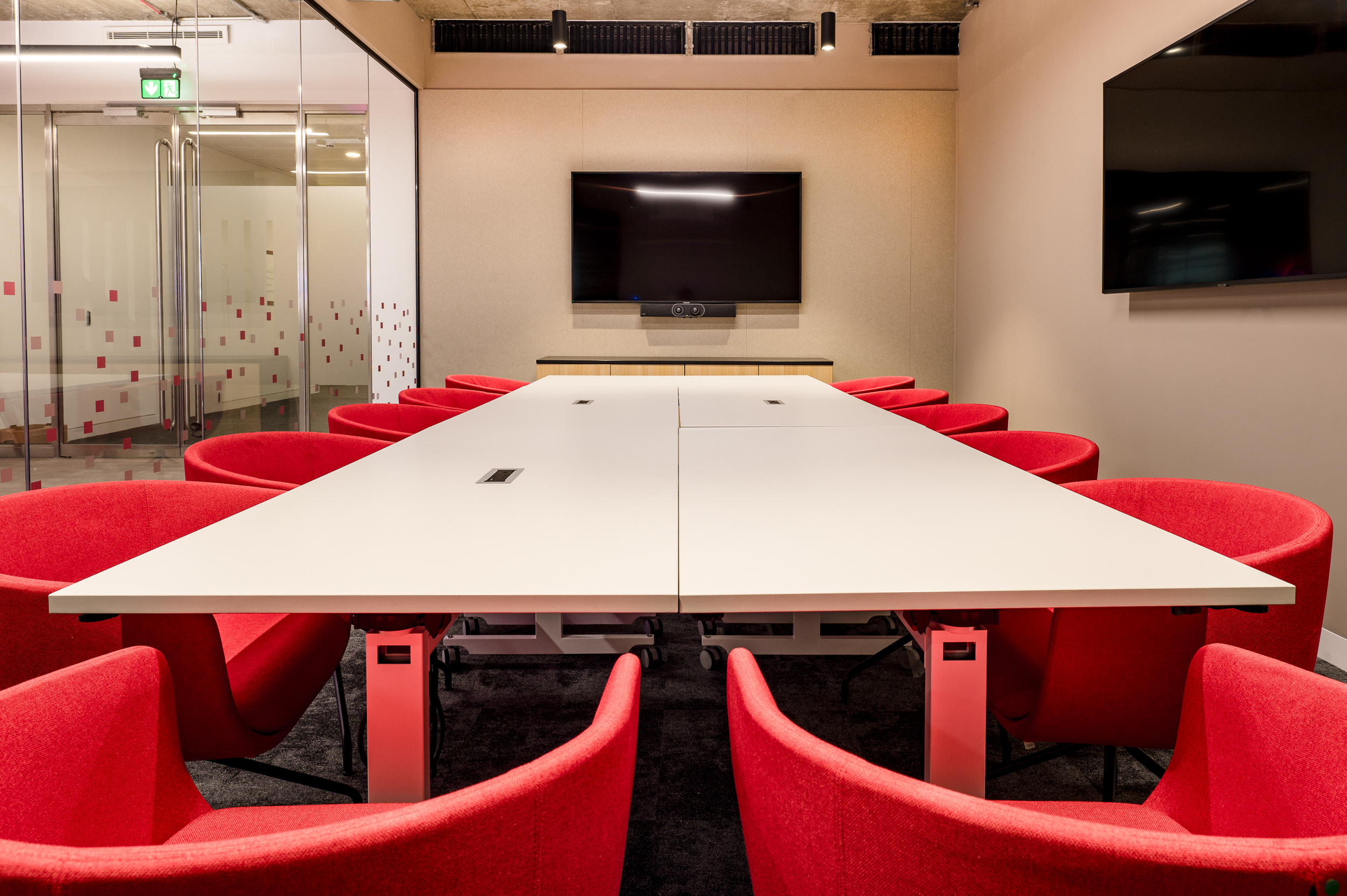 The boardroom in the MicroStrategy office by Two, equipped with red swivel chairs, a modular table, and advanced video conferencing technology.