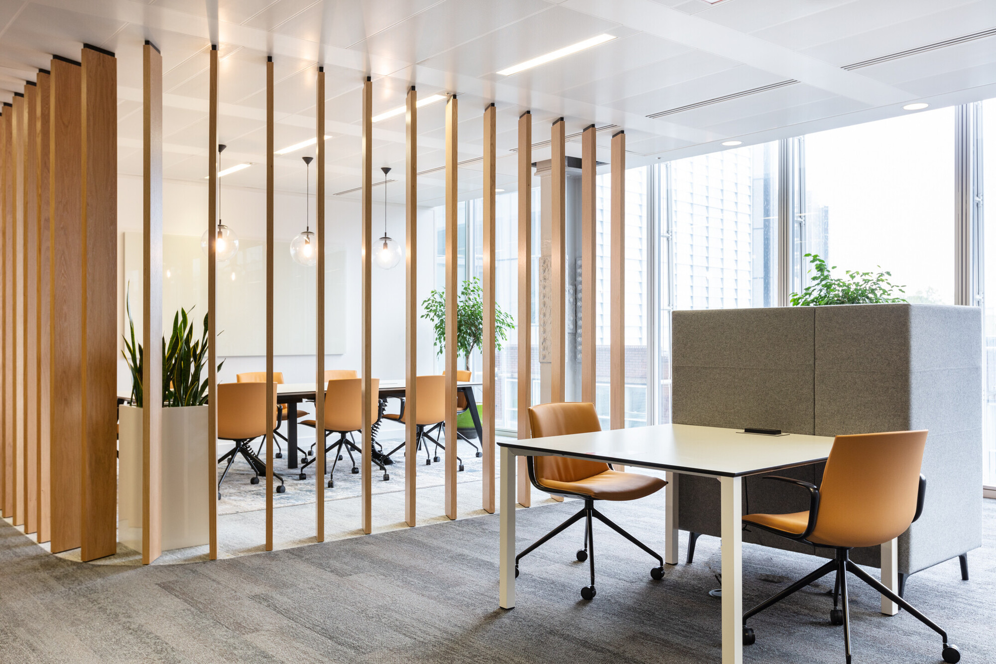 Modern Teradata meeting space designed by Two, showcasing tall wooden slats partitioning the room with ambient lighting. Elegant tan chairs complement the white meeting tables, set in a well-lit office environment.
