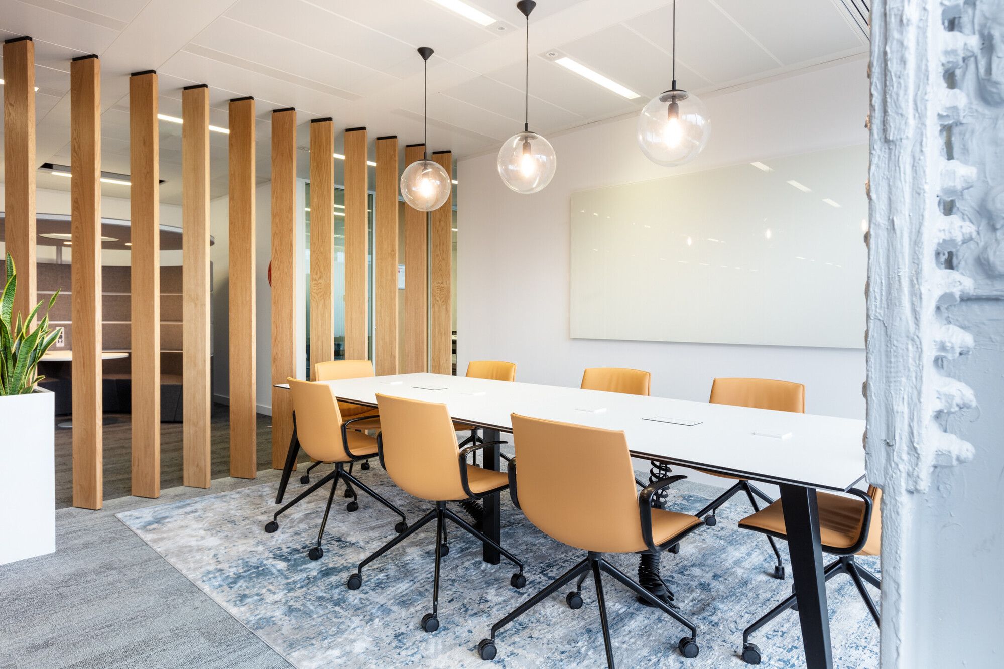 Sleek Teradata office boardroom by Two, highlighted by wooden accents and a large whiteboard. The room is furnished with tan rolling chairs and a long white table, illuminated by stylish hanging lamps.