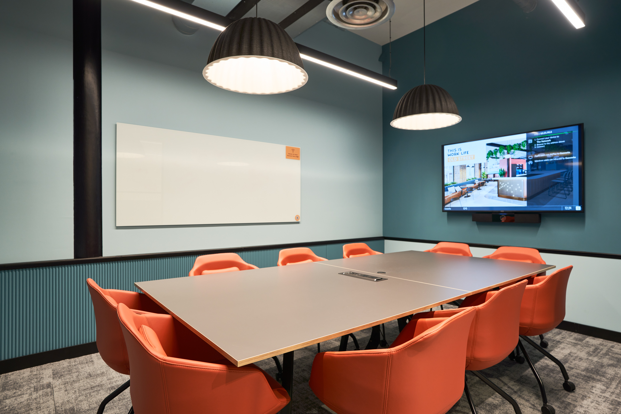 A vibrant meeting room at Work.life Rivington House by Two, featuring a large table, bright orange chairs, and contemporary lighting in a flexible workspace.