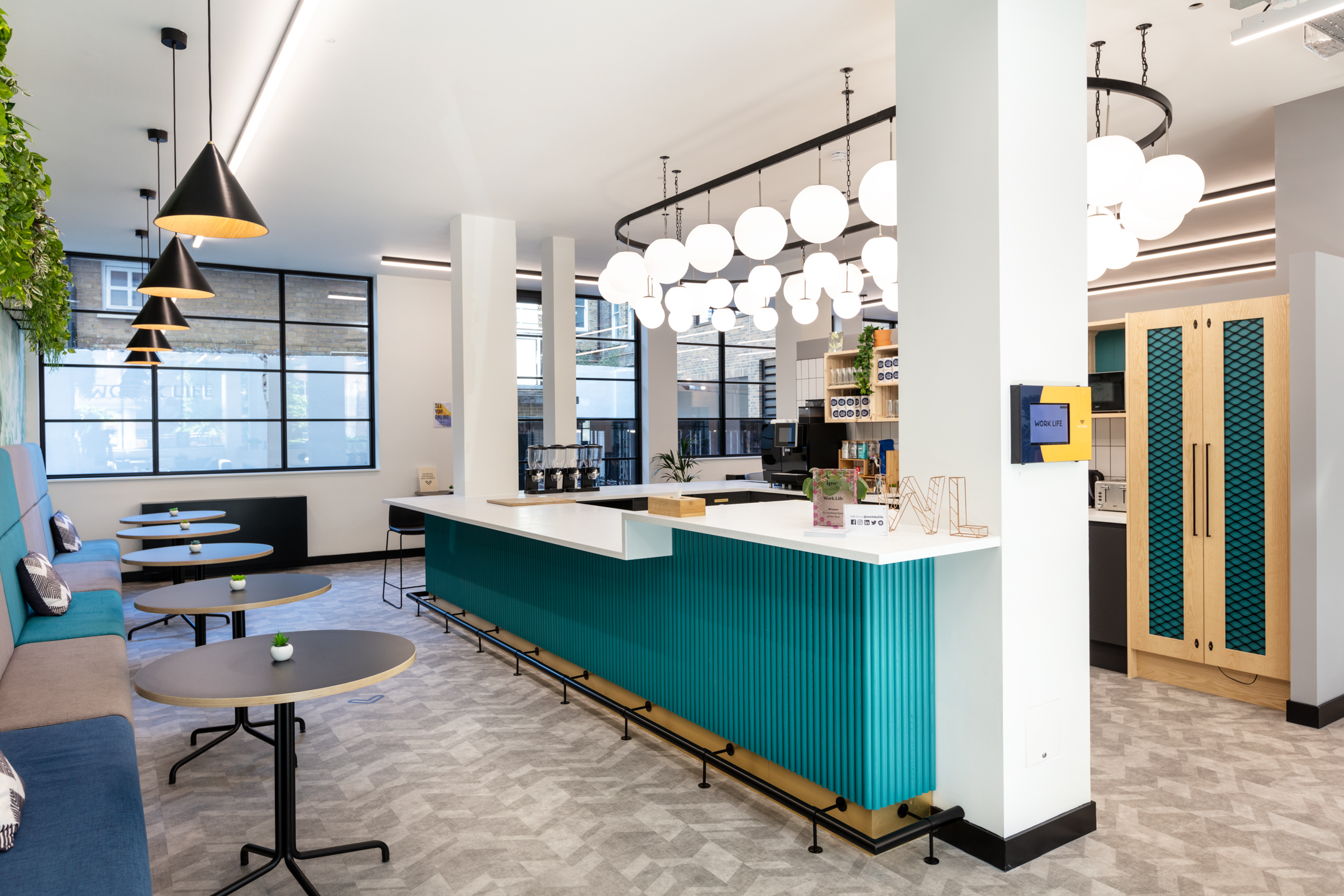 A vibrant communal workspace at Work.life Red Lion Street featuring a sleek turquoise bar counter, stylish pendant lighting, and cosy seating, designed to inspire productivity and collaboration by Two.