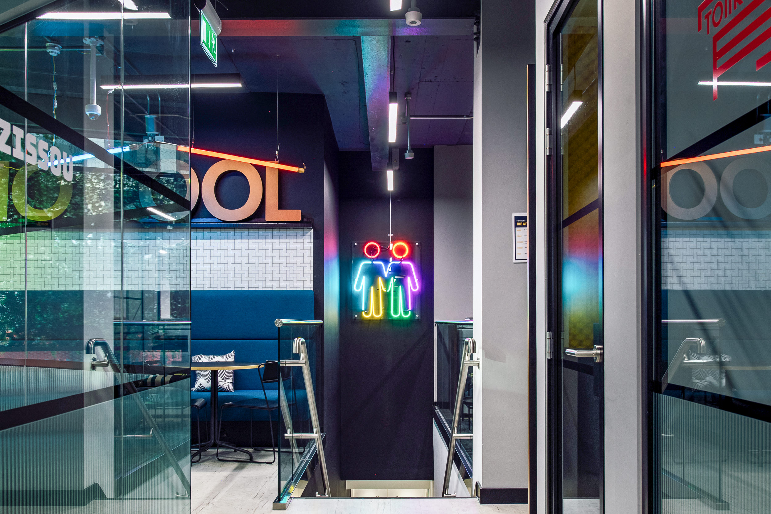 A staircase at Work.life Soho leading to a vibrant workspace, with colourful neon signs and modern industrial design by Two.