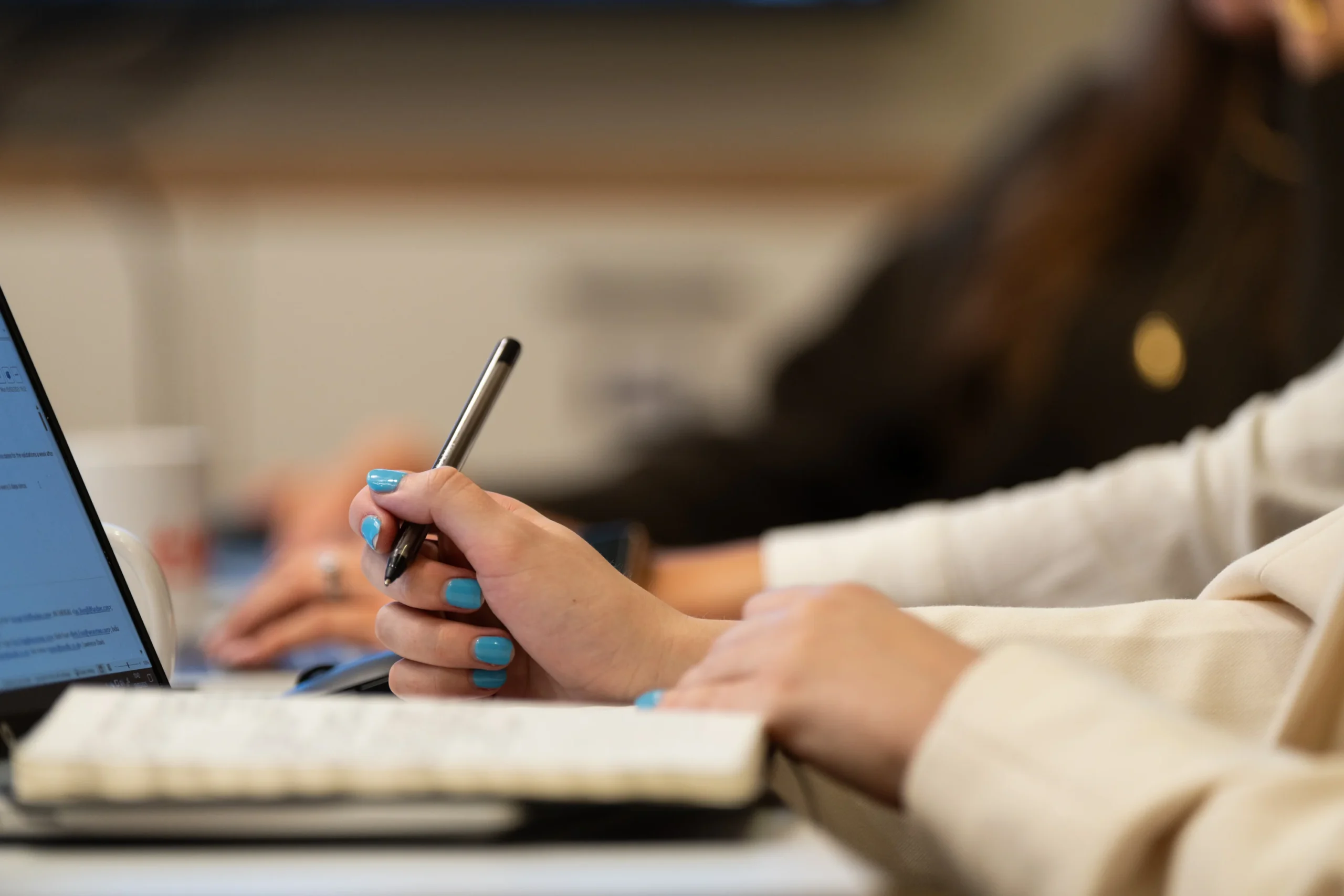 A woman makes notes with her laptop open in front of her